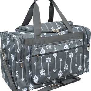 May include: Gray duffel bag with a white arrow pattern. The bag has a top handle, a shoulder strap, and multiple zippered compartments. The bag is designed for travel and has a rectangular shape.