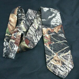 May include: A camouflage patterned tie with brown, green and white colours. The tie is made of a silky fabric and has a pointed tip.