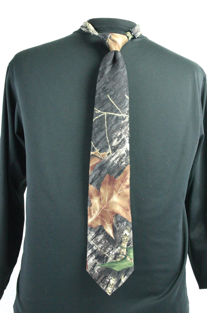 May include: A camouflage patterned tie with brown and green leaves. The tie is tied around a black shirt.