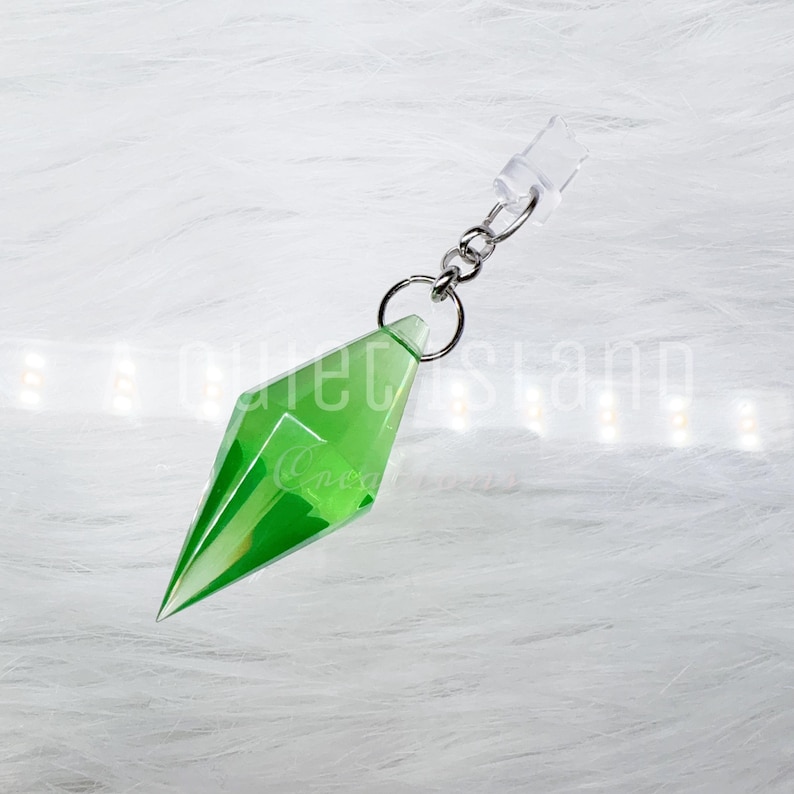 May include: A translucent, bright green, diamond-shaped pendant with faceted edges, attached to a silver-toned metal jump ring and a short chain link. The pendant features a sharp, pointed bottom and a wider, angular middle section.