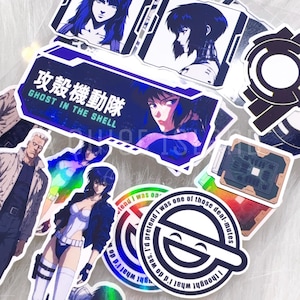 Peut inclure: Une collection d'autocollants Ghost in the Shell représentant des personnages d'anime, le logo Laughing Man avec du texte, et un autocollant rectangulaire avec le texte japonais 攻殻機動隊 et anglais GHOST IN THE SHELL. Les autocollants présentent divers motifs bleus, blancs et noirs.