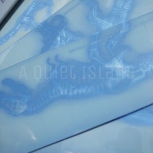 May include: Pale blue art prints featuring a detailed, stylized illustration of a creature. The prints have a layered effect with a lighter blue background. The text "A Quiet Island" is visible on the bottom of the prints.