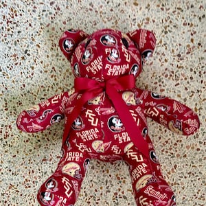 May include: A red teddy bear with a red bow. The bear is covered in a pattern of the Florida State Seminoles logo. The logo is in gold and black.