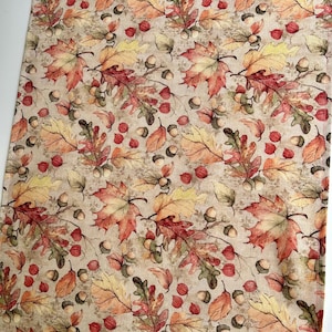May include: A beige fabric table runner with a repeating pattern of autumn leaves in shades of red, orange, yellow, and green. The leaves are interspersed with small brown acorns.