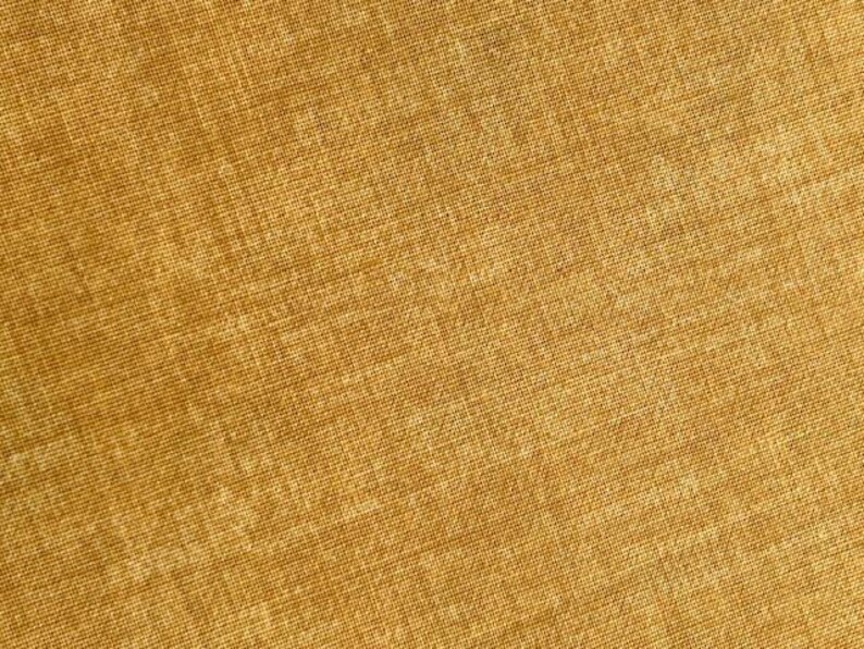 May include: Close-up of a textured, golden-yellow fabric. The weave of the material is visible, creating a subtle pattern of intersecting lines. The color is consistent throughout the image, suggesting a solid-colored textile.