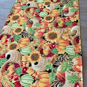 May include: A rectangular table runner with a colorful autumn harvest pattern. The design features sunflowers, pumpkins, gourds, cornucopias, and fall leaves in shades of orange, yellow, red, and green on a black background.