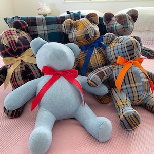 May include: Six plush teddy bears made from plaid fabric. The bears are arranged on a pink and white striped blanket. The bears have different colored bows tied around their necks.