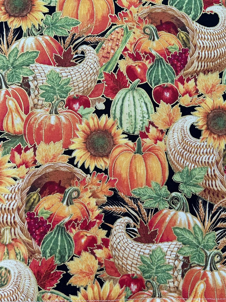 May include: A colorful autumn-themed fabric design featuring pumpkins, sunflowers, cornucopias, and fall foliage. The pumpkins are orange, green, and yellow, with red apples and grapes scattered throughout. The background is black.