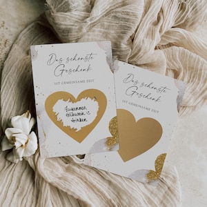 Può includere: Due carte bianche con accenti di glitter dorati e una forma di cuore dorata. Il testo sulle carte recita "Das schonste Geschenk", che si traduce in "Il regalo più bello". Il testo sotto il titolo recita "IST GEMEINSAME ZEIT", che si traduce in "È tempo condiviso". Una carta ha una forma di cuore con il testo "Zusammen Glühwein trinken", che si traduce in "Bere insieme il vin brulè".