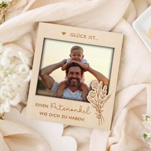 Könnte beinhalten: Ein hellfarbiger Holzbilderrahmen mit einem Foto eines Mannes und eines Kindes. Der Rahmen hat deutschen Text und ein Blumendesign. Das Foto zeigt einen Mann, der ein Kind auf seinen Schultern trägt. Der Text lautet "Glück ist... einen Patenonkel wie dich zu haben!"