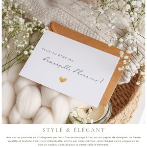 May include: A white card with gold foil accents and the text "VEUX-TU &Ecirc;TRE MA demoiselle d'honneur?"  The card is sitting on a brown envelope and a white knitted blanket.