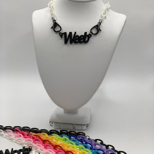 May include: A black plastic necklace with the word "Weeb" spelled out in bold letters. The necklace is on a white mannequin. Below the mannequin are multiple colorful plastic chains.