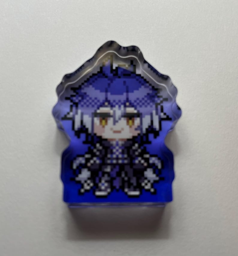 May include: A pixelated acrylic charm featuring a character with blue hair and yellow eyes. The charm has a blue gradient background and a unique, wavy edge. The character is dressed in black clothing.