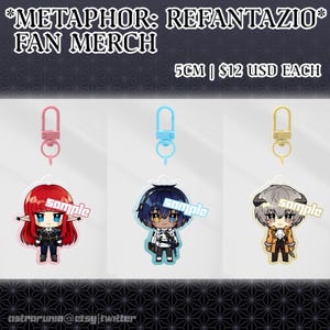 May include: Fan merchandise featuring three character keychains. Each keychain has a different character design with a pink, blue, and gold clasp. The keychains are approximately 5cm in height. The text "METAPHOR: REFANTAZIO FAN MERCH" is at the top.