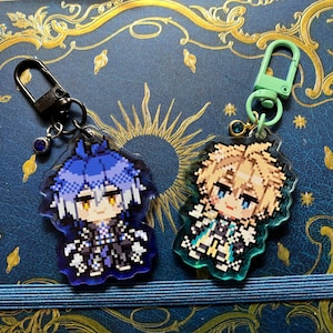 May include: Two pixel art character keychains. One keychain has a black clasp and a blue-haired character. The other keychain has a green clasp and a blonde-haired character. Both keychains are on a blue background with gold accents.