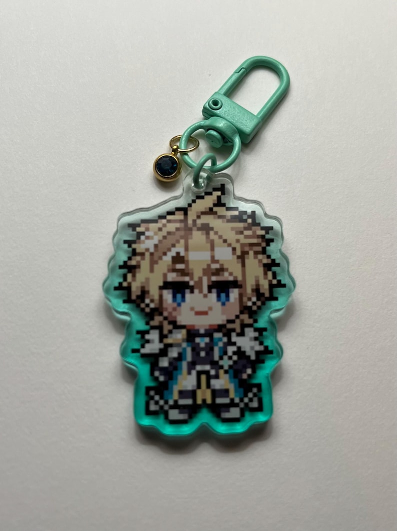 May include: A pixelated anime-style character keychain. The character has blonde hair and blue eyes, with a teal border. The keychain includes a teal clasp and a small gold charm with a dark blue gem. The overall design is colorful and detailed.