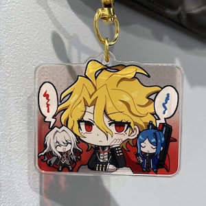 May include: A clear acrylic keychain featuring three anime-style characters with large eyes and detailed outfits. The central character has spiky yellow hair and a black suit. The keychain is attached to a gold-colored metal clasp.