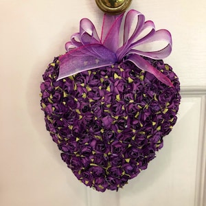 May include: A purple heart-shaped wreath made of small paper roses with a purple and pink ribbon bow.