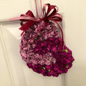 May include: A heart-shaped arrangement of pink and purple paper flowers with a burgundy ribbon bow.