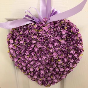 May include: A heart-shaped wreath made of purple paper flowers. The wreath is decorated with a lavender ribbon.
