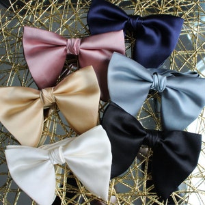May include: Six bow ties in different colors and fabrics, including pink, beige, blue, black, and white. The bow ties are arranged on a gold-colored background.