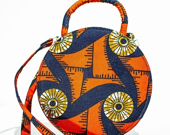 May include: A round orange and blue patterned crossbody bag with a top handle. The bag has a geometric design with a repeating pattern of circles and lines.