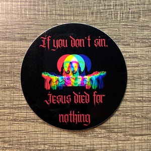 May include: A round black sticker with the text "If you don't sin, Jesus died for nothing" in red gothic font. The sticker features a colorful, layered image of Jesus with outstretched arms, set against a backdrop of red, yellow, and blue circles.