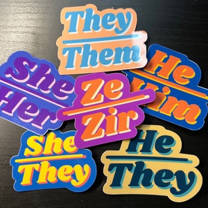 May include: A collection of colorful stickers with gender pronouns. The stickers feature phrases like "They Them", "She Her", and "He Him" in a retro font. The stickers are in shades of blue, orange, purple, and yellow.