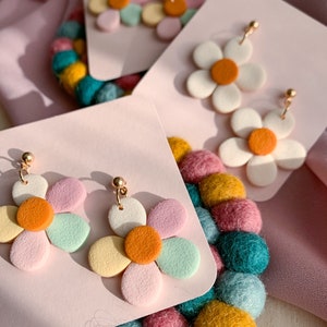 Könnte beinhalten: Ein Paar pastellfarbene Ohrringe in Blumenform mit einem goldenen Haken. Die Ohrringe sind aus Polymer Clay gefertigt und haben eine hellrosa, hellgrüne und gelbe Mitte mit einem kleinen orangen Kreis in der Mitte.