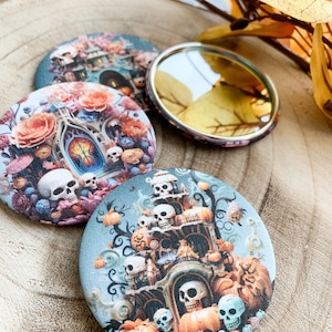 Könnte beinhalten: Drei runde Kompaktspiegel mit Halloween-Motiven. Ein Spiegel hat ein Totenkopf- und Kürbisdesign, ein anderer ein Spukhaus mit Kürbissen und Totenköpfen, und der dritte ist ein einfacher Spiegel.