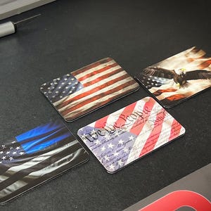 May include: Four rectangular magnets with patriotic designs. The first magnet features a red, white, and blue American flag. The second magnet features a bald eagle with its wings spread wide. The third magnet features the text "We the People" with a red, white, and blue background. The fourth magnet features a blue and white police flag.