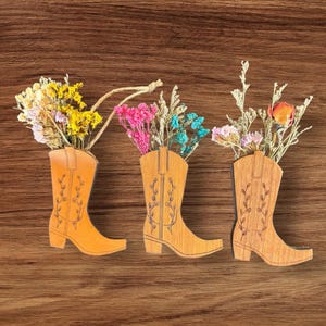 May include: Three wooden cowboy boot ornaments with dried flowers in them. The boots are brown and have a floral design. The flowers are yellow, pink, and blue.