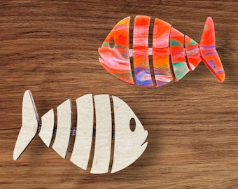 Pode incluir: Duas formas de peixe de madeira, uma pintada com redemoinhos laranja, vermelho e verde e a outra pintada de branco com listras pretas.