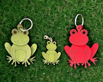 Pode incluir: Três chaveiros de couro em forma de sapo. Um é vermelho e os outros dois são verdes. O chaveiro de sapo vermelho tem um anel prateado. Os chaveiros de sapo verdes têm anéis prateados e são de tamanhos diferentes.