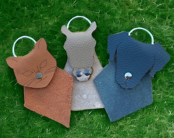 Pode incluir: Três porta-chaves de couro em forma de animal com argolas de metal. Um gato castanho, um cavalo bege e um cão azul escuro. Cada porta-chaves possui um fecho de mola e uma superfície texturizada para guardar as chaves com segurança.
