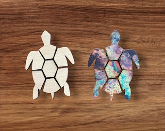 Pode incluir: Dois quebra-cabeças de madeira em forma de tartaruga. Uma tartaruga é de madeira clara natural com veios visíveis, enquanto a outra apresenta um padrão iridescente vibrante e multicolorido com redemoinhos de azul, roxo, rosa e verde no casco.