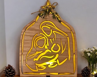 Pode incluir: Um presépio de madeira com um design recortado de Maria, José e o menino Jesus. A cena é iluminada por trás, criando um brilho quente. A madeira é de cor castanho claro.