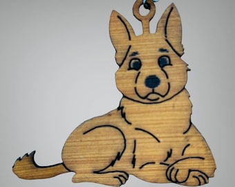 Pode incluir: Enfeite de madeira em forma de cão pastor alemão. O cão está deitado com as orelhas levantadas. O enfeite é feito de madeira castanha clara com detalhes pretos e uma pequena argola para pendurar.