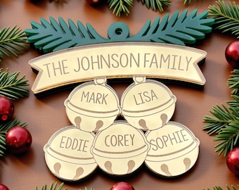 Pode incluir: Um enfeite de Natal personalizado com o texto "THE JOHNSON FAMILY" acima de cinco enfeites em forma de sino. Cada sino é gravado com um nome: Mark, Lisa, Eddie, Corey e Sophie. O enfeite é rodeado por ramos de pinheiro e enfeites vermelhos.