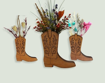 Pode incluir: Três bolsos de parede de madeira em forma de bota de cowboy com padrões decorativos de volutas gravados a laser. Cada bota serve como recipiente para vários arranjos de flores secas, incluindo caules e ervas vermelhas, amarelas, azuis e rosas.