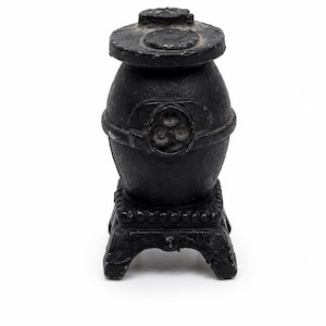 May include: A small, black cast iron potbelly stove miniature featuring a rounded body, a circular top plate with a central lid, and a square base with four short legs. The front of the stove displays a circular emblem with three small circles.