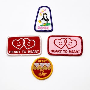 May include: Four embroidered patches: a trapezoidal patch with a penguin and the text DANCE, two rectangular patches with two smiling hearts and the text HEART TO HEART, and a circular patch with three hearts and the text HEART TO HEART.