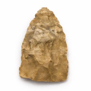 May include: A tan-colored stone arrowhead featuring a pointed tip and a wide, flat base. The surface displays a textured, chipped appearance with visible flaking patterns across the entire body, creating sharp, irregular edges along the sides.