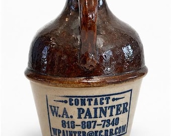 May include: A stoneware jug with a dark brown glazed upper section and a light tan lower section. A single handle is attached to the top. The front features blue printed text: CONTACT W.A. PAINTER 818-807-7340 WPAINTER@KC.RR.COM inside a rectangle.
