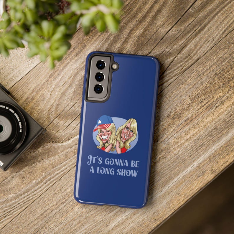 Pu&ograve; includere: Una custodia per telefono blu con un'immagine di cartone animato di due donne e il testo "It's gonna be a long show".