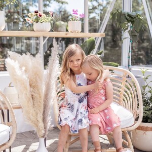 Young girl twirling a sleeveless Summer dress featuring a large vintage inspired palm leaf design with peachy orchids and creamy roses. Think vintage palm springs with a touch of the tropics. Square shaped back and a full twirl skirt