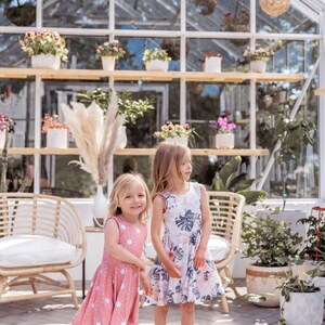 Young girl twirling a sleeveless Summer dress featuring a large vintage inspired palm leaf design with peachy orchids and creamy roses. Think vintage palm springs with a touch of the tropics. Square shaped back and a full twirl skirt