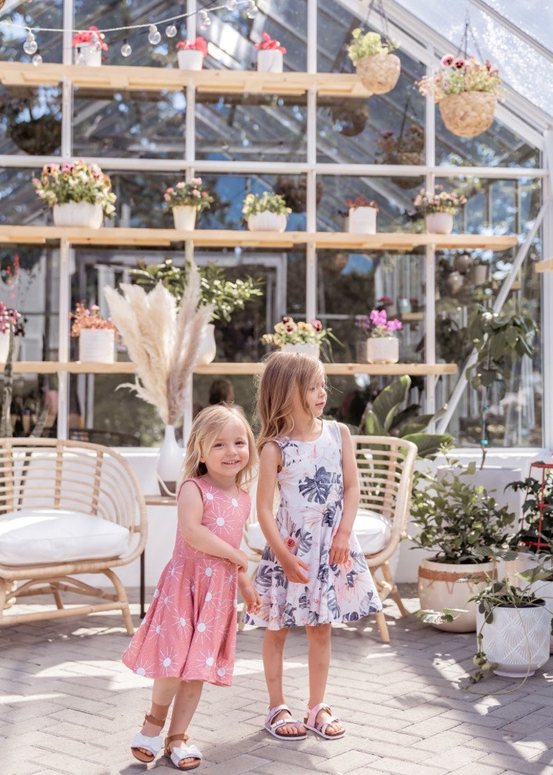 Young girl twirling a sleeveless Summer dress featuring a large vintage inspired palm leaf design with peachy orchids and creamy roses. Think vintage palm springs with a touch of the tropics. Square shaped back and a full twirl skirt