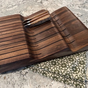 Può includere: Un portacoltelli in legno marrone scuro con un design curvo e più fessure per contenere i coltelli. Il blocco è in legno di noce e ha una finitura naturale.