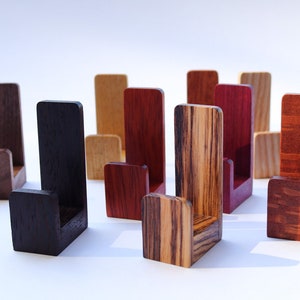May include: A collection of wooden display stands in various wood tones, including dark brown, reddish brown, and light brown. The stands are shaped like a letter J and have a small shelf at the top.